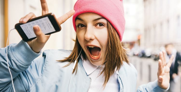 Ung tjej i rosa mössa håller upp en mobil och ropar glatt