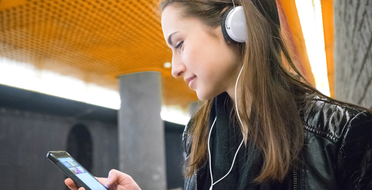 Ung kvinna med hörlurar tittar på sin mobil i tunnelbanan