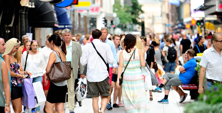 Människor går med shoppingpåsar på en trång gågata en sommardag